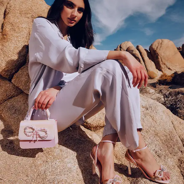 A woman sitting on a rock wearing vegan heels and a handbag from Call It Spring